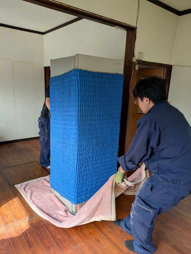 養生した冷蔵庫を毛布に載せて室内から搬出するパワーセラーのスタッフ